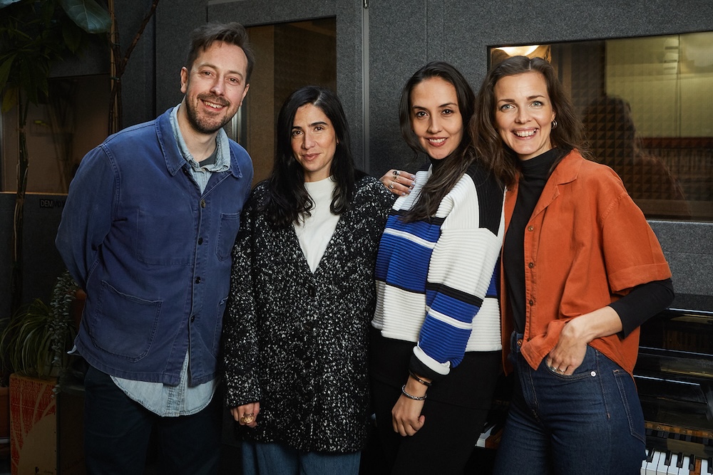 four singing tutors smiling at camera in front of sound booth