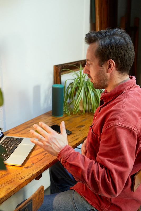 singing teacher sat at a desk giving lesson online on a macbook