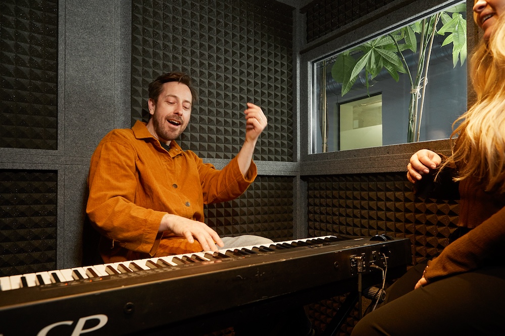 singing teacher playing keyboard in a sound booth with student singing