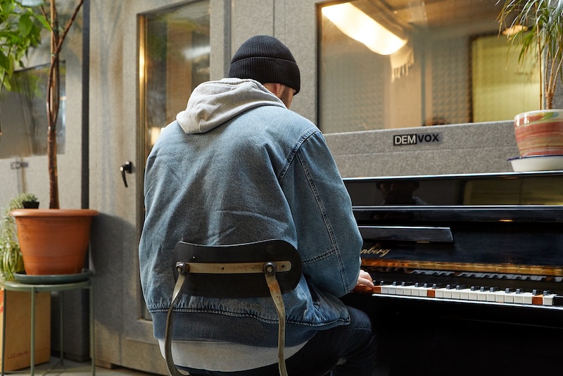 student playing piano in denim jacket with his back to us